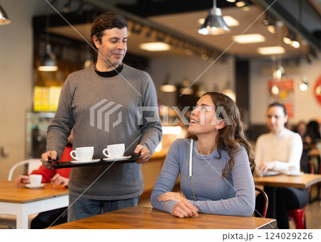 Man with two cups of coffee asks permission to sit at a table next to girl in a cafe Man with two cups of coffee asks permission to sit at a table next to girl in a cafe 124029226