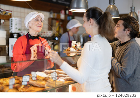 Bakery shop senior female assistant talk to customer, answers questions and recommends fresh products Bakery shop senior female assistant talk to customer, answers questions and recommends fresh products 124029232