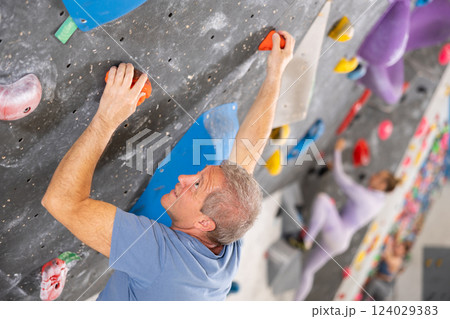 Alpinist practicing indoor rock climbing on artificial boulder without safety belts 124029383