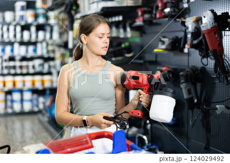 Woman chooses and buys paint spray gun in hardware store 124029492