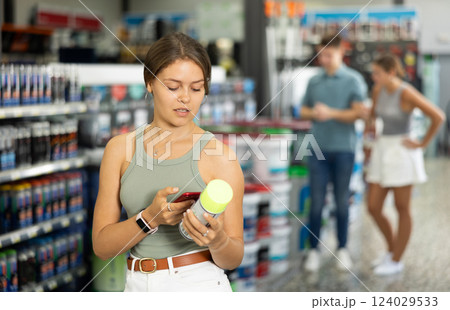 Woman visitor studies information on product label and photographs packaging of product with phone 124029533