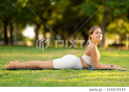 Girl in park on green grass of lawn performs bhujangasana 124029545
