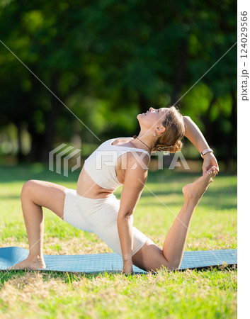 Sporty girl performing Crescent Low Lunge Pose on green meadow 124029566