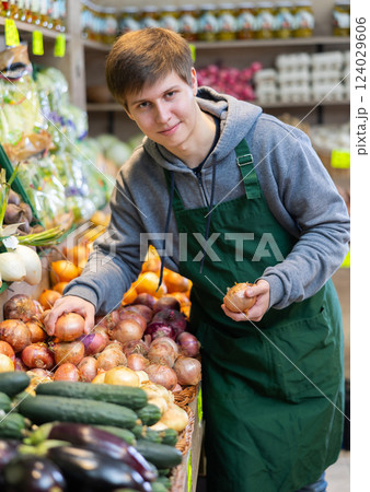 Young male seller putting onions in vegetable basket in grocery market Young male seller putting onions in vegetable basket in grocery market 124029606