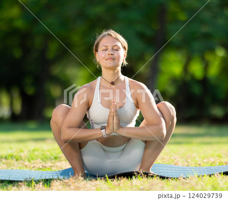 Sporty girl performing yoga asanas on green meadow in summer 124029739