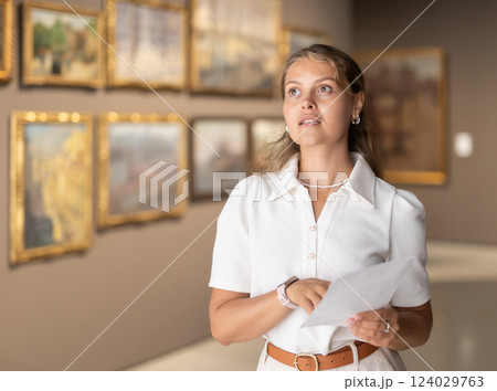 Woman with sheet piece of paper in hands view pictures and icons in museum hall Woman with sheet piece of paper in hands view pictures and icons in museum hall 124029763