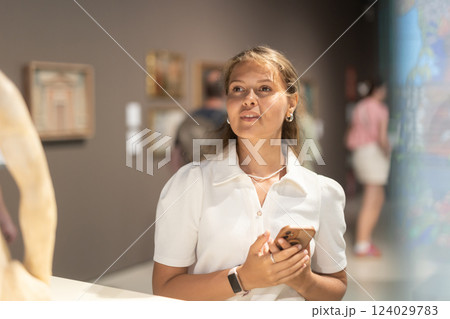 Girl with phone in hands walks around museum hall, view exhibition items 124029783