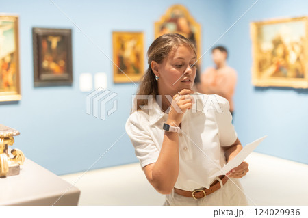 Woman with sheet piece of paper in hands view pictures and icons in museum hall Woman with sheet piece of paper in hands view pictures and icons in museum hall 124029936