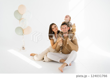 Happy family of three, father, mother and two child boy, are posing for a photo in front of a bunch of balloons 124031766