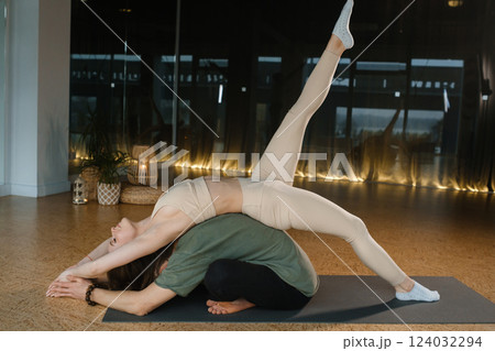 Yoga practice involving a woman executing a challenging pose on a man's back in a modern studio setting during a morning session 124032294