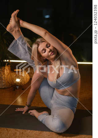Yoga practitioner demonstrates impressive flexibility in serene studio setting during evening relaxation session with soft lighting 124032398