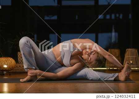 Yoga practitioner performs advanced stretch in serene indoor setting during twilight hours, highlighting flexibility and calmness 124032411