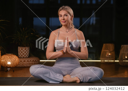 Woman practicing yoga in a modern studio with soft lighting while sitting in a meditative pose and hands in prayer position 124032412