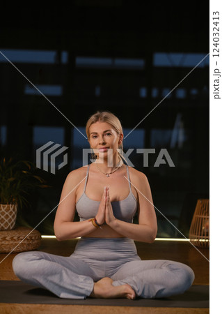 Woman practicing yoga in a modern studio with soft lighting while sitting in a meditative pose and hands in prayer position 124032413