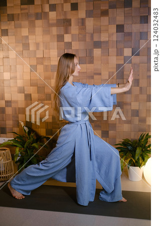 Girl in blue kimano practicing kundalini or qigong yoga in fitness gym . Spiritual energy, life force located at the base of the spine Girl in blue kimano practicing kundalini or qigong yoga in fitness gym . Spiritual energy, life force located at the base of the spine 124032483