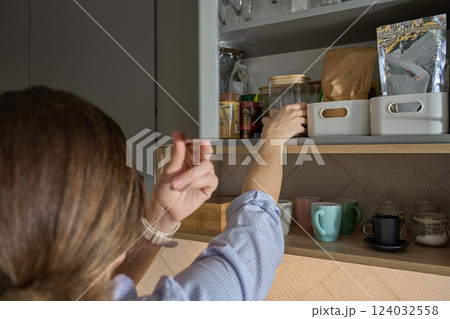 Woman reaching for jar in kitchen cabinet with stored cooking ingredients 124032558