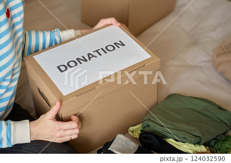 Woman holding donation box with clothes on bed Woman holding donation box with clothes on bed 124032590