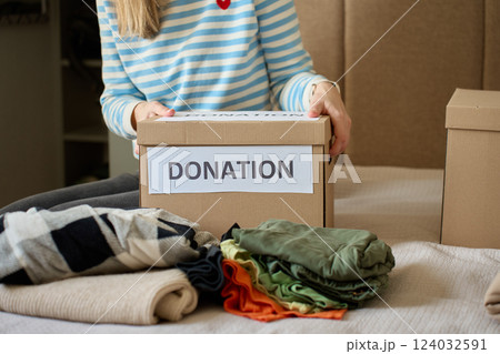 Woman holding donation box with clothes on bed Woman holding donation box with clothes on bed 124032591