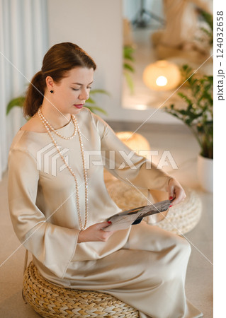 Girl in beige dress with beads with a fan of Tarot cards indoors . Tarot cards in the hands of a fortune teller Girl in beige dress with beads with a fan of Tarot cards indoors . Tarot cards in the hands of a fortune teller 124032658