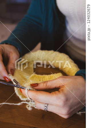 Women hands holding knitting needles and yellow cotton knitted work. Knitting woman with bobbins of yarn and yellow knitwear. Needlework in process. Knitting hobby. Knitter work.  124032679