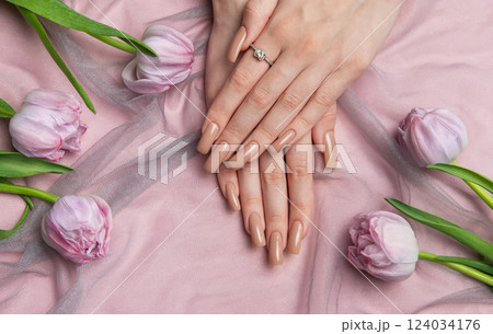 Woman showing nude manicure with engagement ring near pink tulips Woman showing nude manicure with engagement ring near pink tulips 124034176