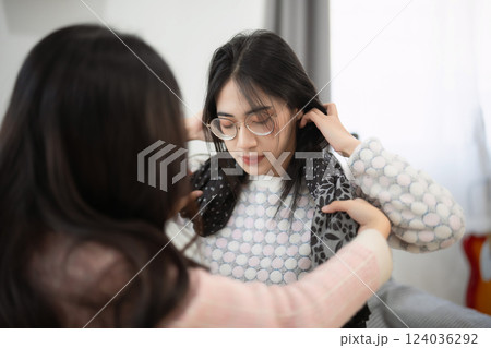 Two young women engaging in a cozy indoor activity as one styles the hair of the other, reflecting friendship and shared moments at home Two young women engaging in a cozy indoor activity as one styles the hair of the other, reflecting friendship and shared moments at home 124036292