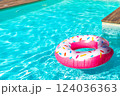 Pink donut-shaped inflatable float in turquoise swimming pool with wooden deck on a sunny day 124036363
