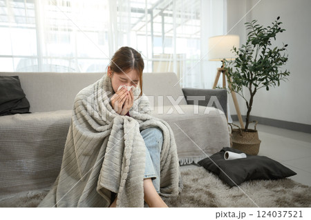 Unwell asian woman experiencing cold and flu symptoms, sneezing into a tissue Unwell asian woman experiencing cold and flu symptoms, sneezing into a tissue 124037521