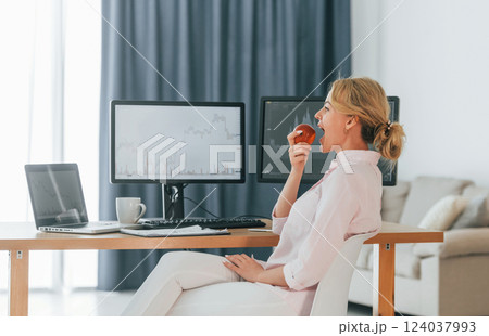 Eating an apple. Female stock broker in formal wear is working in the office Eating an apple. Female stock broker in formal wear is working in the office 124037993