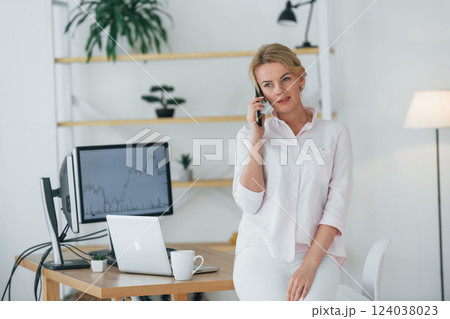Using smartphone to communicate. Female stock broker in formal wear is working in the office 124038023