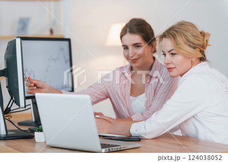 Talking with each other. Two female stock brokers in formal wear is working in the office by pc Talking with each other. Two female stock brokers in formal wear is working in the office by pc 124038052