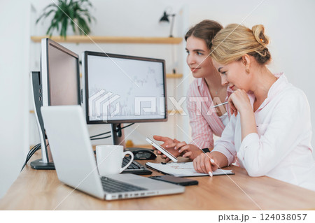 Using phone. Two female stock brokers in formal wear is working in the office by pc Using phone. Two female stock brokers in formal wear is working in the office by pc 124038057