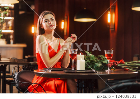 Woman in red dress sitting alone in the restaurant. Flowers and candles Woman in red dress sitting alone in the restaurant. Flowers and candles 124038533