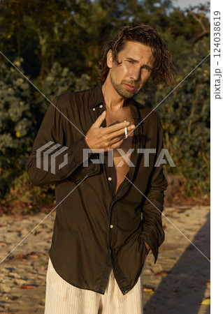 smoking boy on the beach at sunset. handsome wet man walking on sand smoking boy on the beach at sunset. handsome wet man walking on sand 124038619