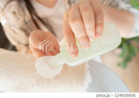 A woman pours nail polish remover onto a cotton pad, preparing for a manicure and nail care routine at home. A woman pours nail polish remover onto a cotton pad, preparing for a manicure and nail care routine at home. 124038656