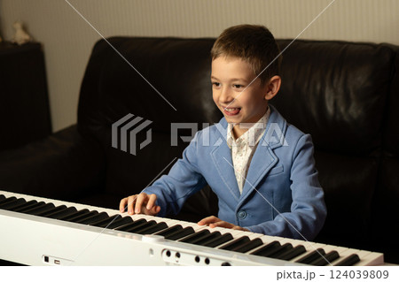 Cheerful young boy in blue blazer playing the piano. 124039809