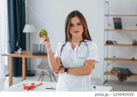 Woman holding an apple. Professional medical worker in white coat is in the office Woman holding an apple. Professional medical worker in white coat is in the office 124040439