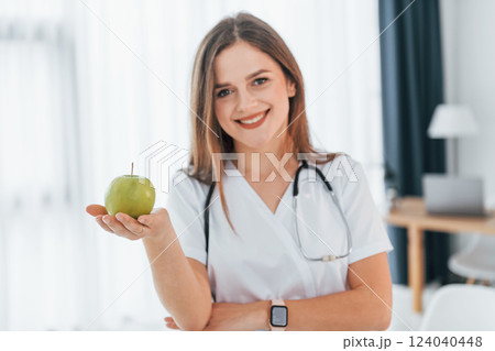 Woman holding an apple. Professional medical worker in white coat is in the office Woman holding an apple. Professional medical worker in white coat is in the office 124040448