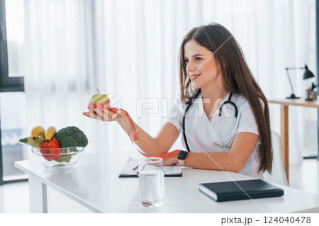 Conception of dieting. Holding apple. Professional medical worker in white coat is in the office 124040478