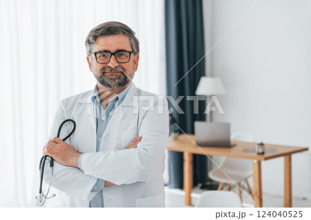Standing and holding stethoscope. Professional medical worker in white coat is in the office 124040525