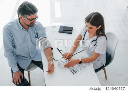 Female doctor is measuring blood pressure of the man. Professional medical worker in white coat is in the office Female doctor is measuring blood pressure of the man. Professional medical worker in white coat is in the office 124040557