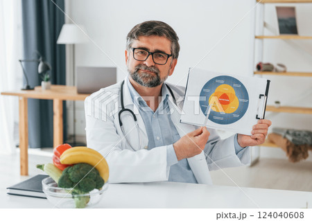 Holding dieting plan illustration. Professional medical worker in white coat is in the office Holding dieting plan illustration. Professional medical worker in white coat is in the office 124040608