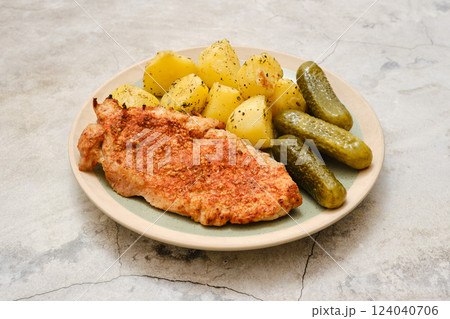 Delicious pork chop served with tender potatoes and pickles on a simple plate Delicious pork chop served with tender potatoes and pickles on a simple plate 124040706