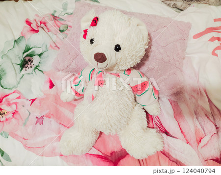 Adorable fluffy white teddy bear in a watermelonprint outfit rests on a pink floral bedspread. Perfect for childrens products, websites, blogs, or illustrating stories about friendship and comfort. Adorable fluffy white teddy bear in a watermelonprint outfit rests on a pink floral bedspread. Perfect for childrens products, websites, blogs, or illustrating stories about friendship and comfort. 124040794