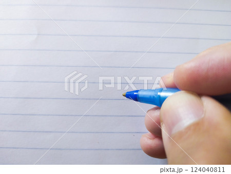 Closeup of a hand holding a blue pen above lined paper.  Perfect for concepts of writing, education, notetaking, or backtoschool themes. 124040811