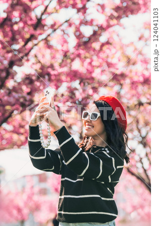 happy woman taking selfie on the phone in front of blooming sakura 124041103