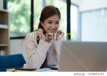 Confident business woman smiling Show successful gestures at her desk with market charts and documents in office Confident business woman smiling Show successful gestures at her desk with market charts and documents in office 124041337