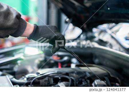 Serviceman checks the oil level in a car engine Serviceman checks the oil level in a car engine 124041377