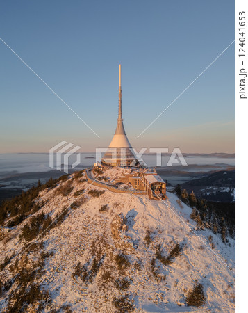 A breathtaking view of Jested Mountain at sunrise, showcasing the snow-covered peak and surrounding landscape. The serene atmosphere highlights the natural beauty during wintertime. 124041653