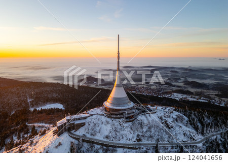 Jested Mountain showcases a stunning winter sunrise, casting warm light over its snowy landscape and the surrounding forest. Jested Mountain showcases a stunning winter sunrise, casting warm light over its snowy landscape and the surrounding forest. 124041656